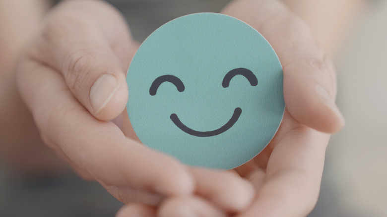 close-up of two hands holding a green smily face