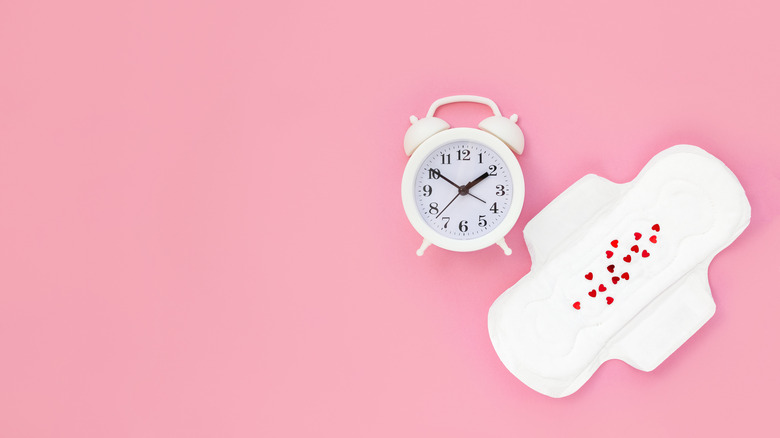 menstrual pad dotted with hearts next to a clock 