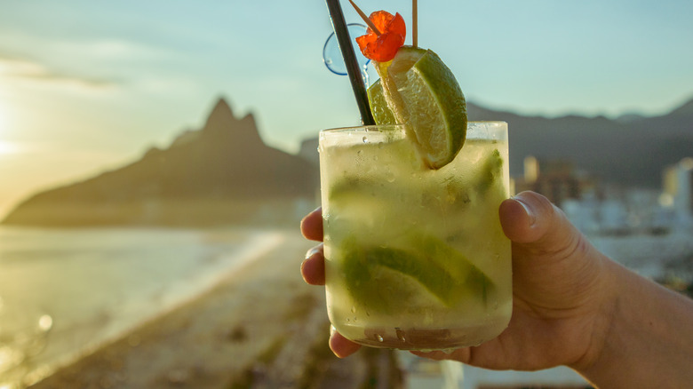 hand holding alcoholic drink with lime on beach
