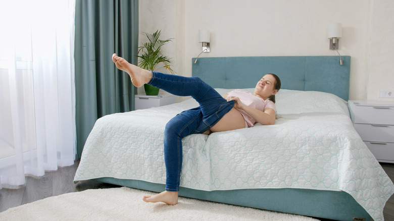 woman on bed pulling up tight jeans