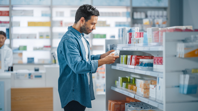 man reading supplement box in pharmacy