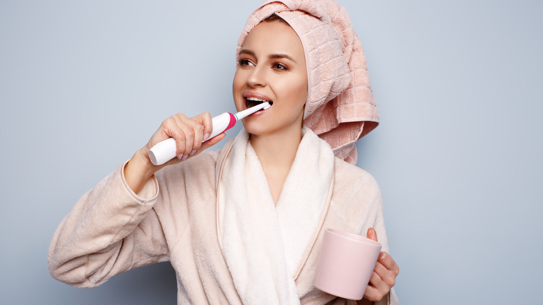 woman holding coffee brushing teeth