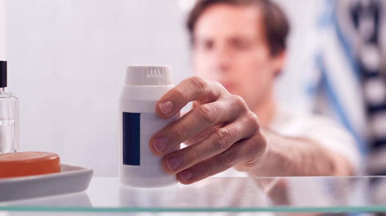 man reaching for pill bottle in cabinet