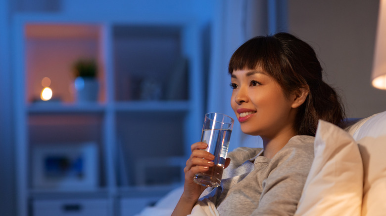 woman sitting in bed at night drinking a glass of water 