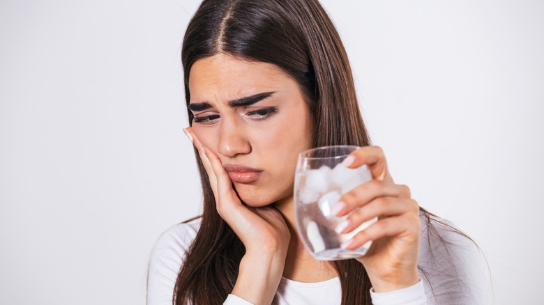 Woman holding her face with a glass of iced water