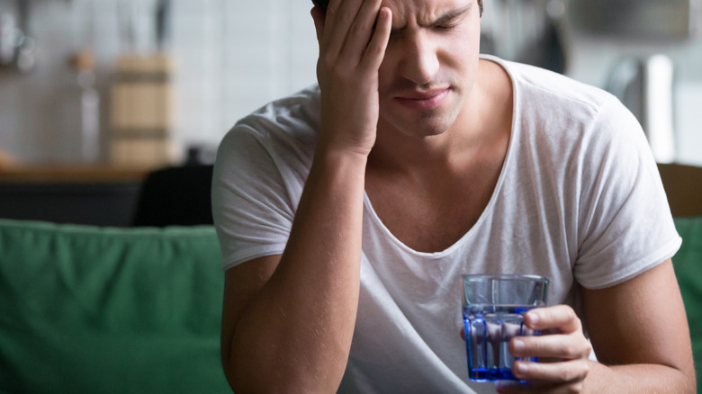 man looking stressed holding a cup of water