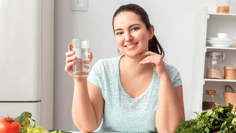 woman holding a glass of water leaning over a table of produce
