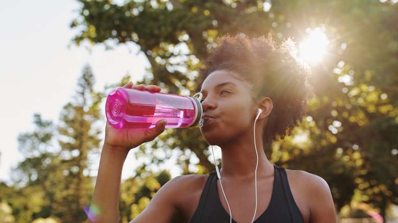 black woman drinking water out of a bottle while exercising outdoors