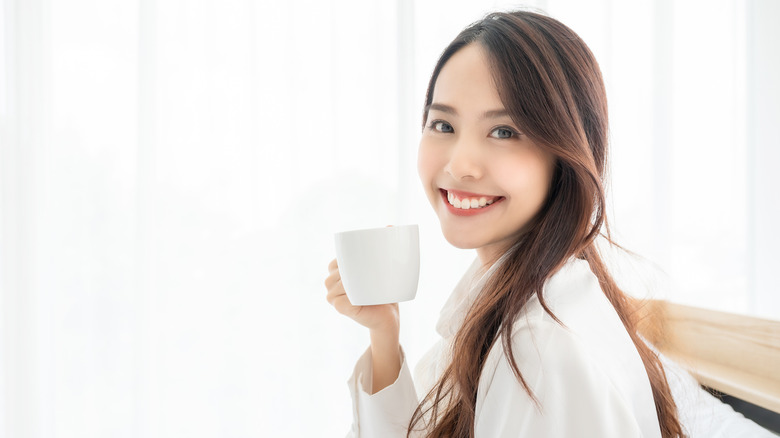 woman in bed smiling with a mug