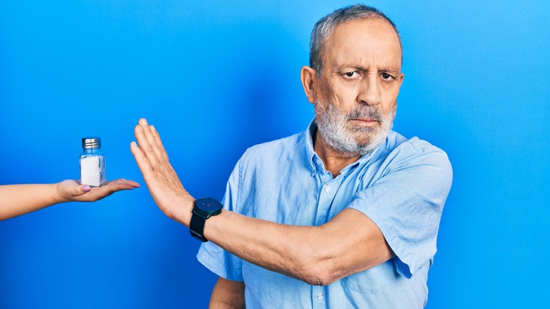 elderly man holding up hand next to salt shaker