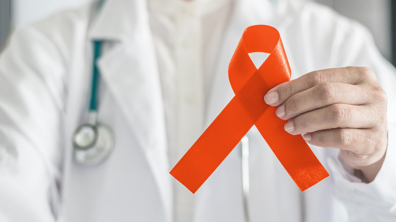 The chest and arm of a doctor holding the orange multiple sclerosis ribbon toward the camera