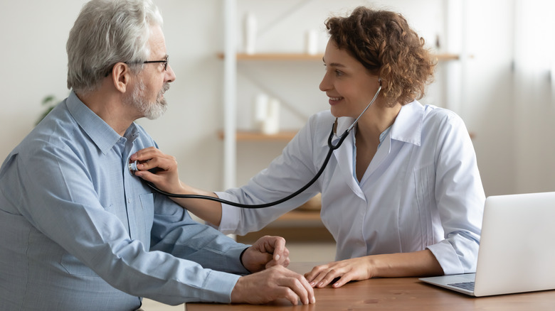 female doctor listening to the heart of an older man