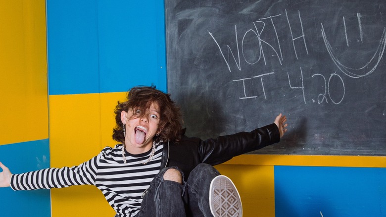 Jacob Sartorius sitting in front of a blue and yellow wall and a chalkboard that says 'Worth It 4.20 :)'