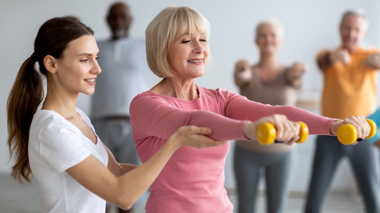 physical trainer helping woman lift weights