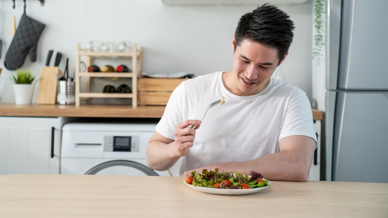 man eating salad in kitchen