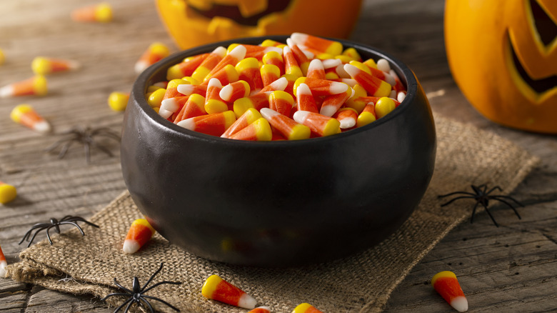 A bowl of candy corn next to Halloween pumpkins