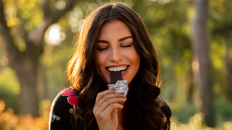 A woman taking a bite from a dark chocolate bar