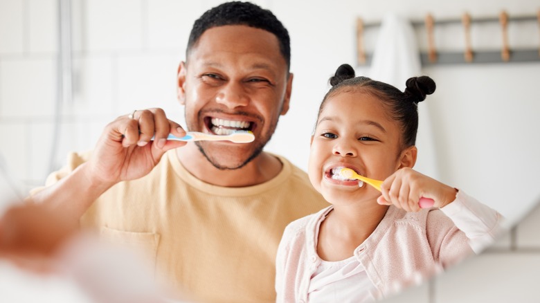 A father and his daughter brushing their teeth while looking in the mirror