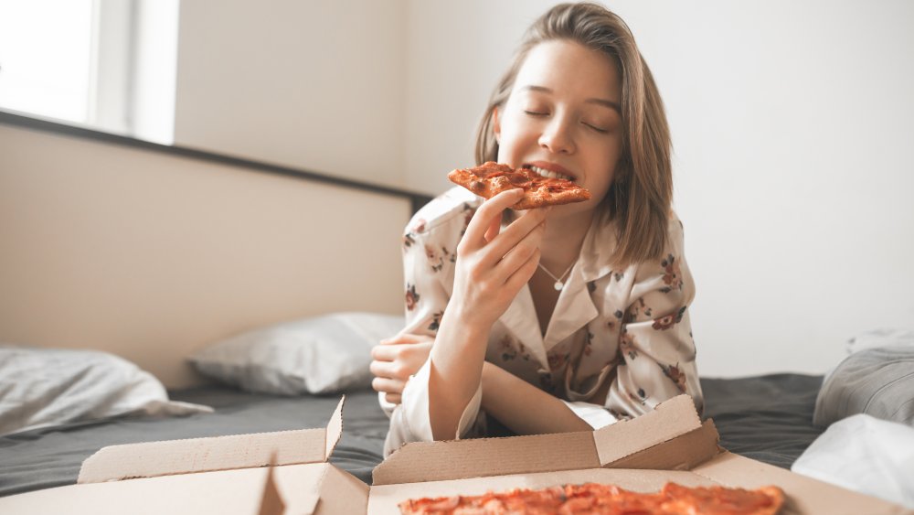 woman eating pizza in bed