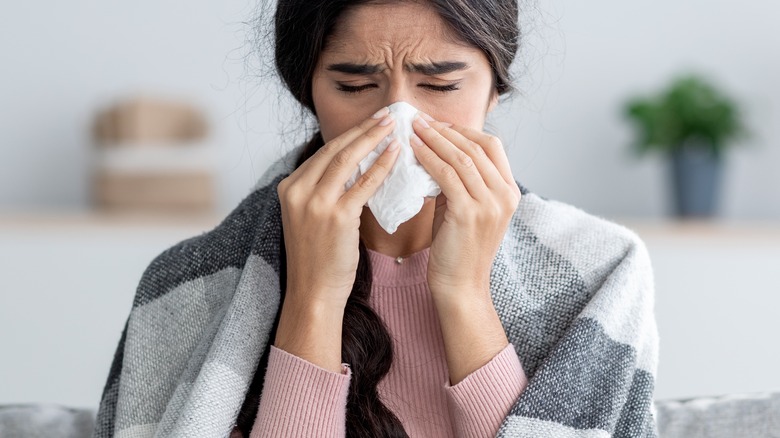 Woman on couch blowing her nose