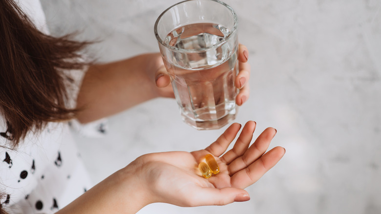 Person holding water glass and supplements