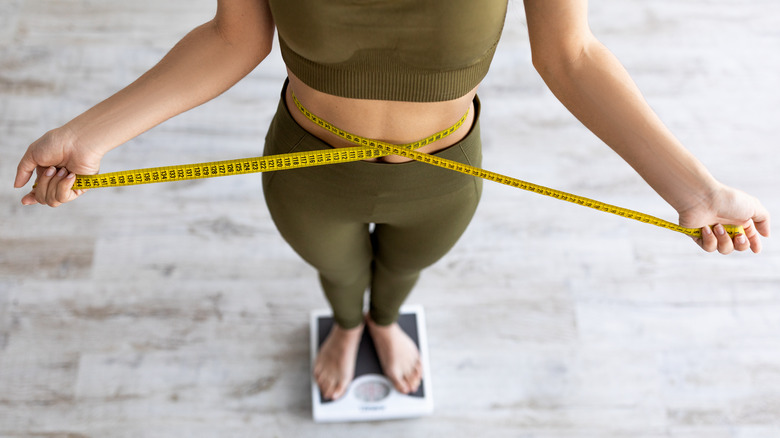 woman measuring waist while standing on scale