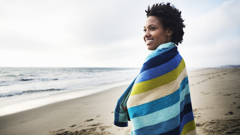 Woman standing on beach wrapped in towel