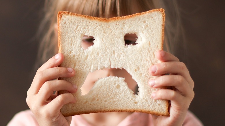 girl holding up slice of bread like a mask