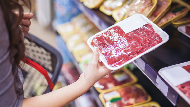 Woman holding package of meat in grocery store