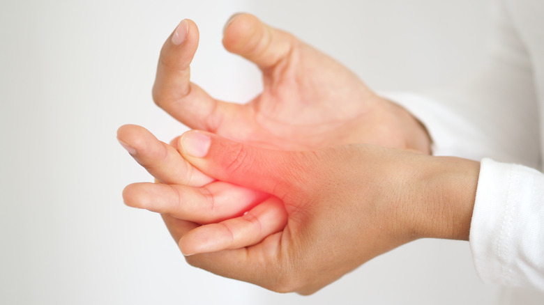 Woman rubbing her hand with red highlight indicating joint pain