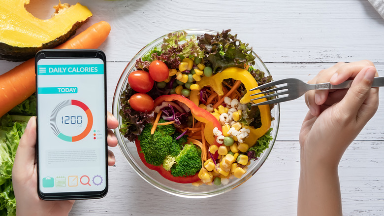 Woman counting calories while eating a salad