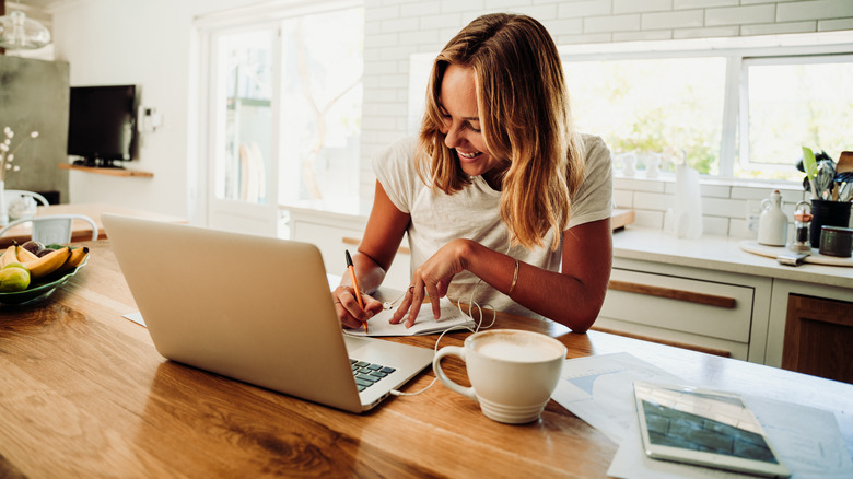 woman working in kitchen with laptop and coffee