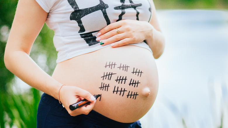 woman marking due date on her pregnant belly