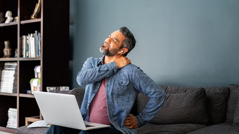 Man with laptop holding neck
