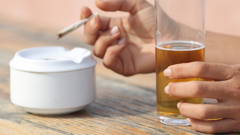 person holds cigarette and alcoholic drink