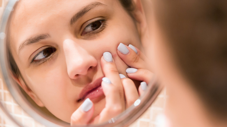 woman looks into mirror and squeezes pimple 