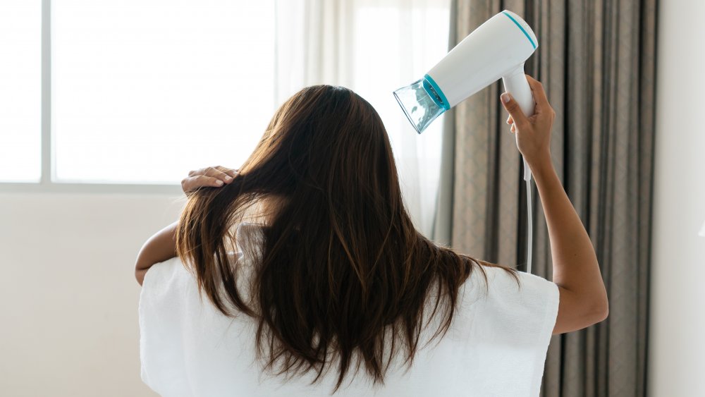 a woman in her bathrobe blow drying her hair 