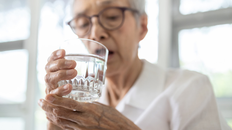 An elderly woman holds a glass of water