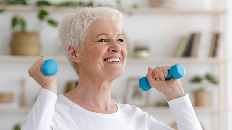 Older woman lifting small blue weights over shoulders