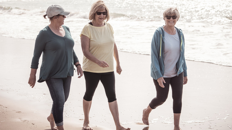 Three older women walk on the beach