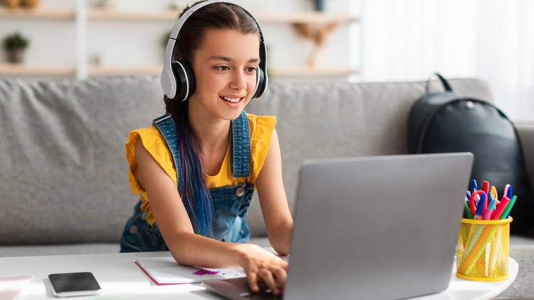 young girl with headphones playing a video game on her laptop