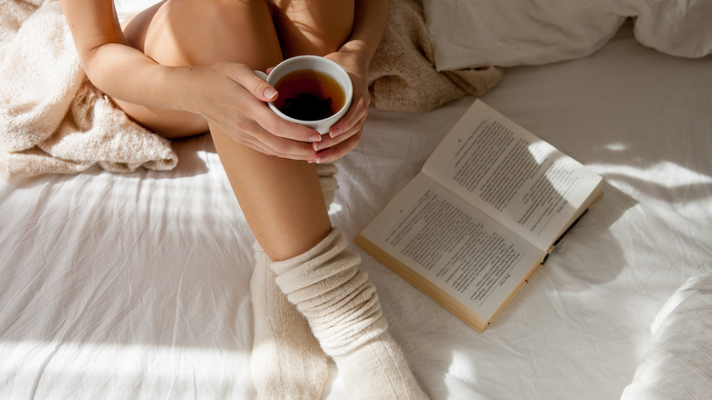 woman holding cup of tea in bed 