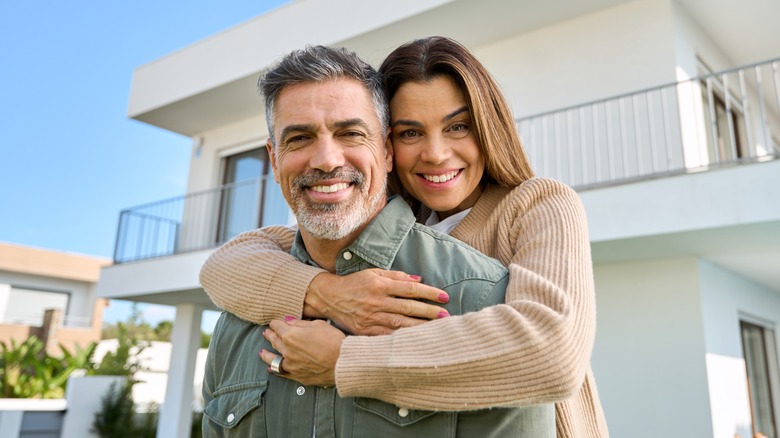 A happy middle-aged couple holding each other outside their home