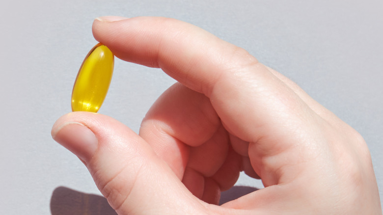 Hand holds up an omega-3 capsule against a gray background