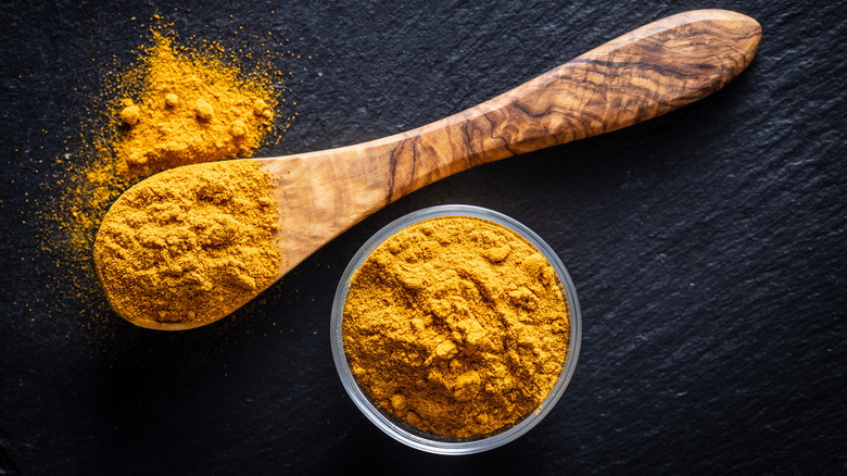 Ground turmeric in a bowl and in a wooden spoon against a black background