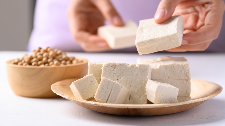 Blocks of tofu on a plate with bowl of chickpeas in the background
