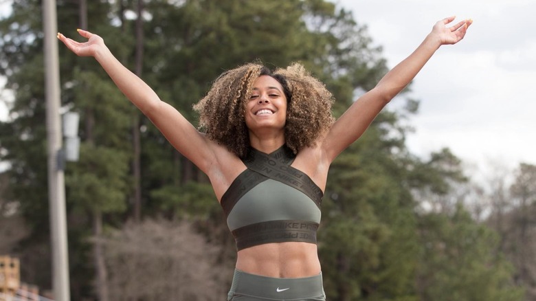 Gabbi Cunningham stands on a track with a huge smile and her arms extended above her head in celebration