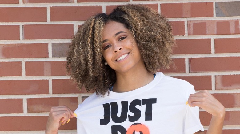 Gabbi Cunningham wearing a "Just Do It" Nike shirt standing in front of brick wall, smiling