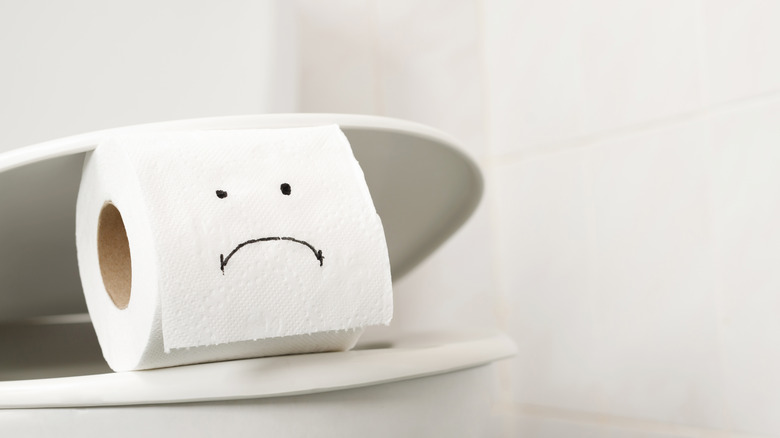 toilet paper with frown face, placed on toilet bowl