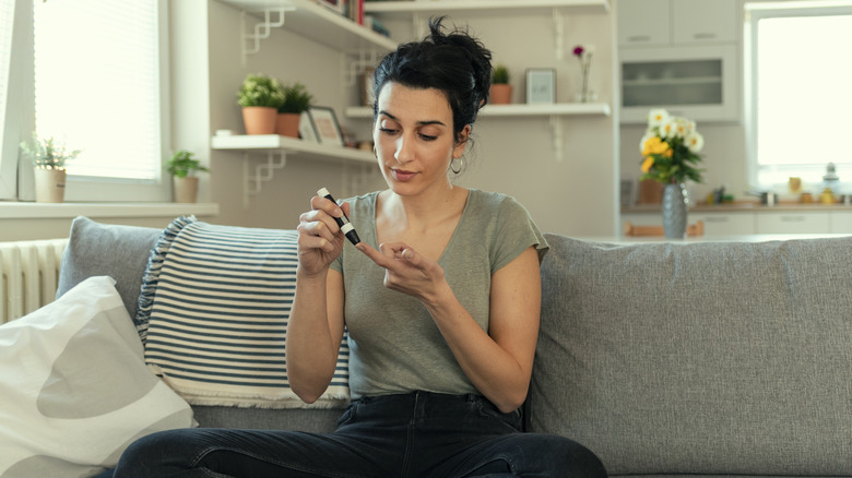 woman testing blood sugar on couch